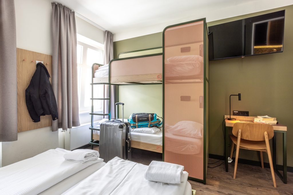 Dorm room with red furniture and a standing luggage next to a bunk bed