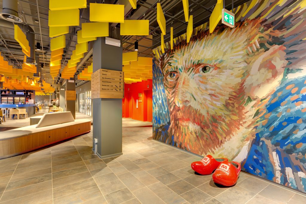 Hotel lobby with yellow ceiling panels, a Van Gogh mural and big red clogs