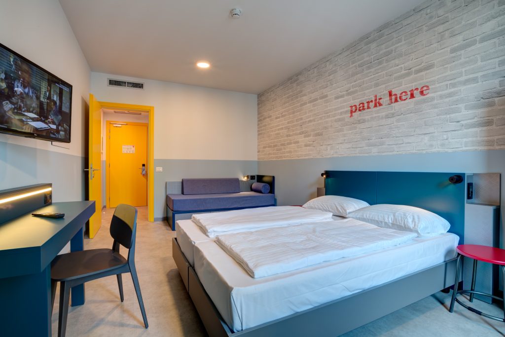 Double bed and sofa bed in a bright room with red park here wall lettering