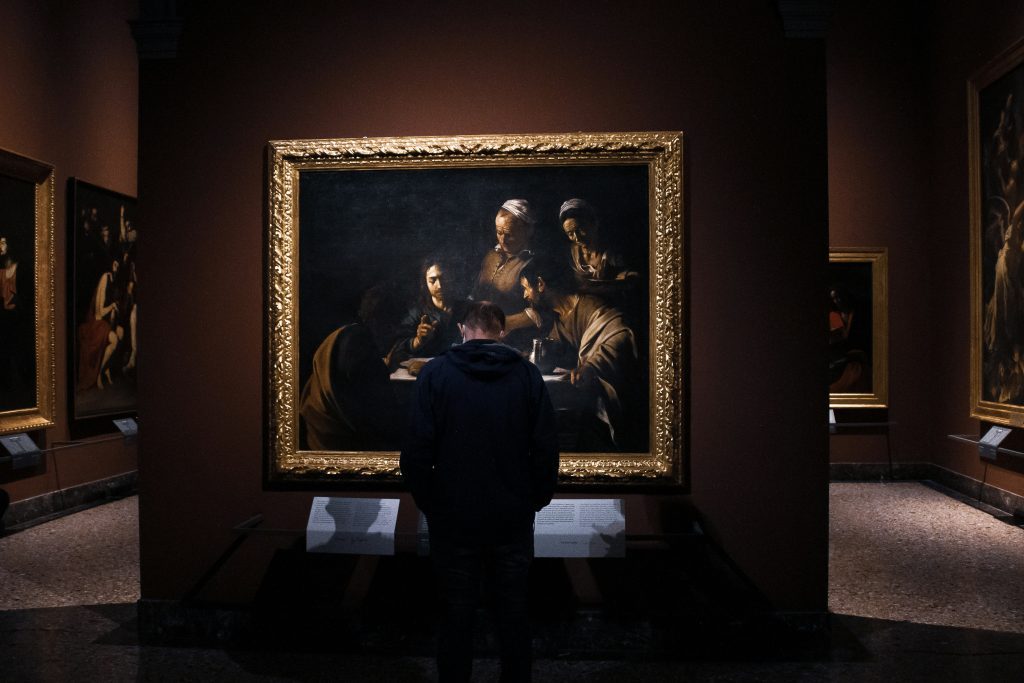 Man looking at a gold-framed painting in a dim room at Pinacoteca di Brera