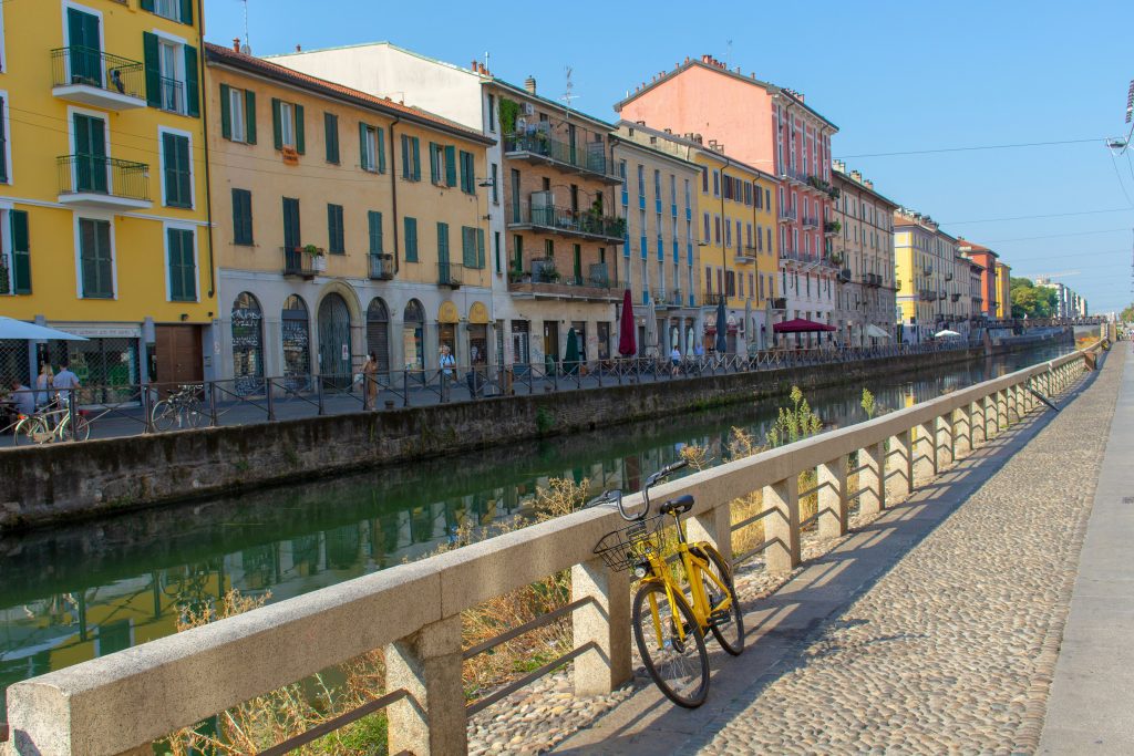 Yellow bike parked along the Navigli canal in Milan, lined with pastel houses