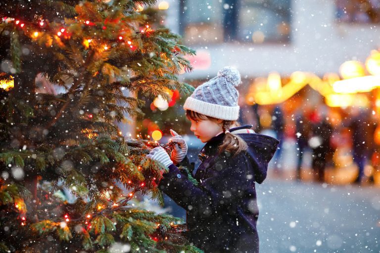 A little girl in winter cloths at a Christmas market next to a Christmas tree