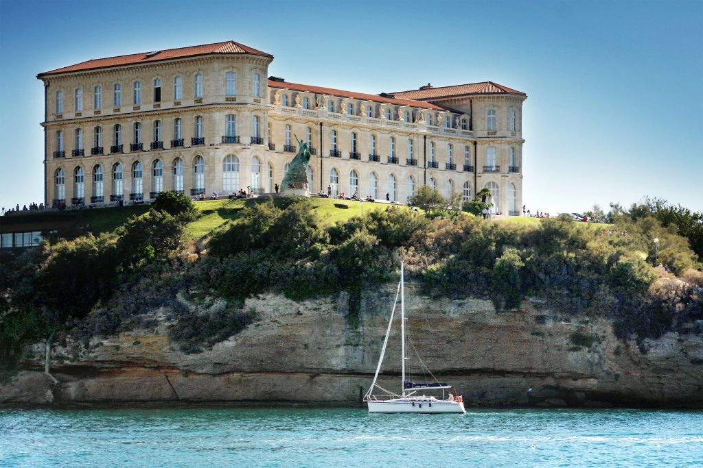 Sailboat below Palais du Pharo and sunny gardens on a winter day in Marseille
