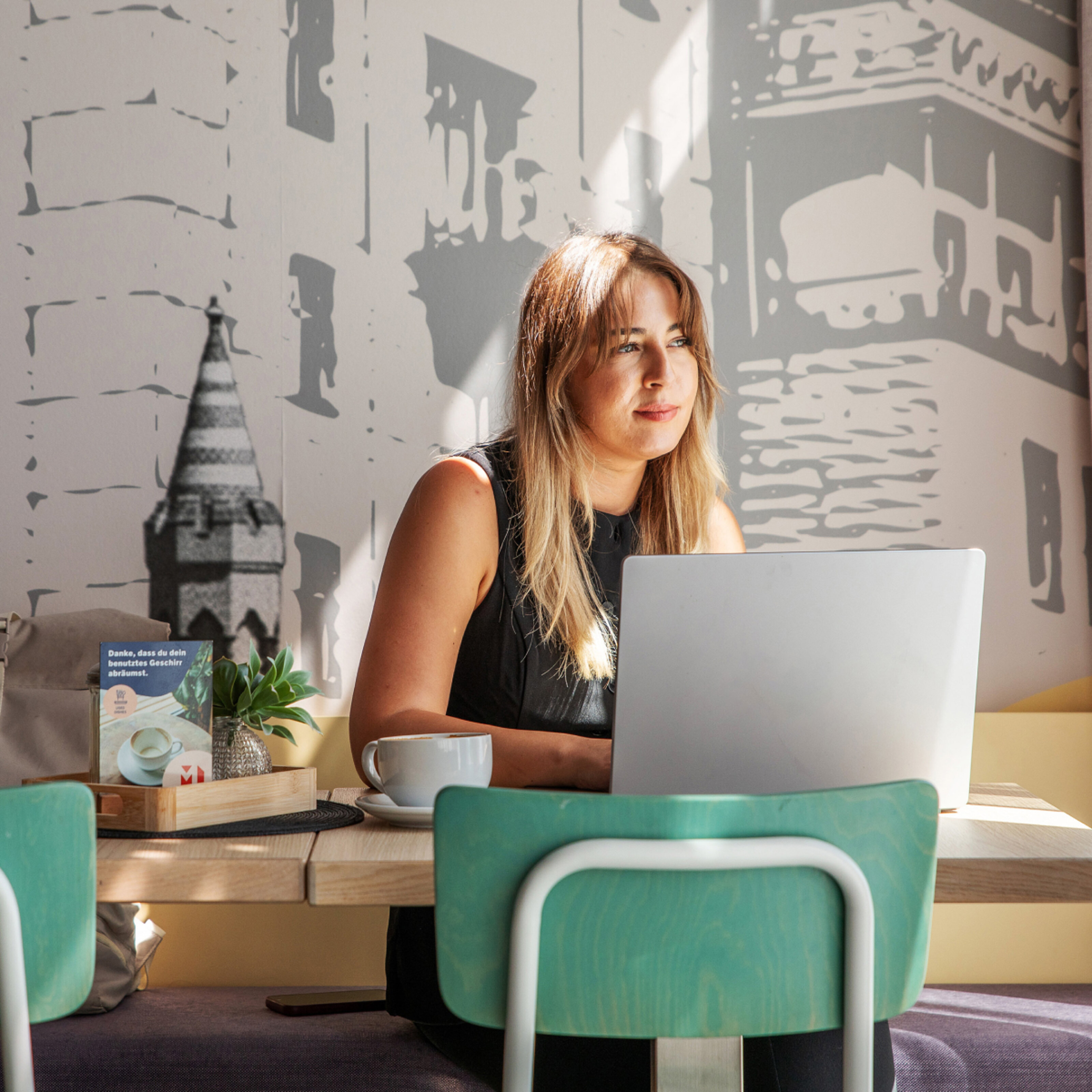 Eine Frau mit Laptop sitzt in der Lobby des MEININGER Hotels