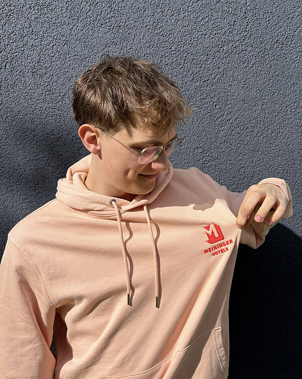 A portrait of Jonsman with a MEININGER Hotels branded peach hoodie