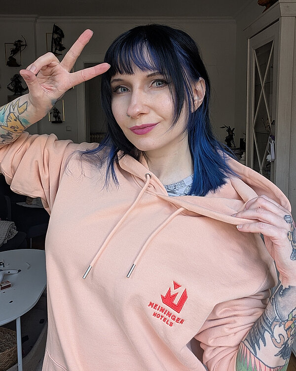 A portrait of Rikku with a MEININGER Hotels branded peach hoodie