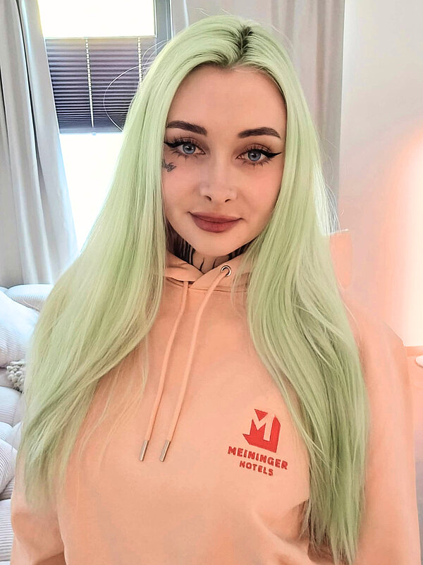 A portrait of EdenNymph with a MEININGER Hotels branded peach hoodie